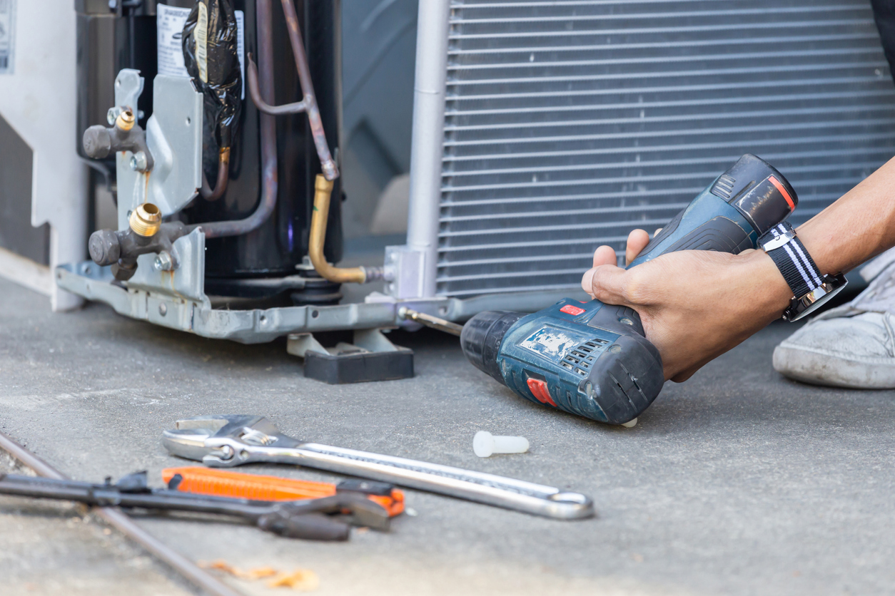 Person using a power drill to repair air conditioning unit on concrete floor.