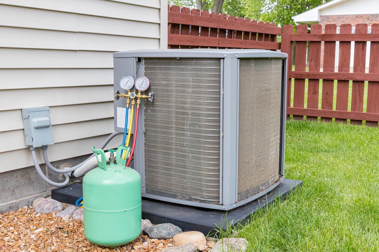 Air conditioning unit with pressure gauges and refrigerant tank in backyard setting.