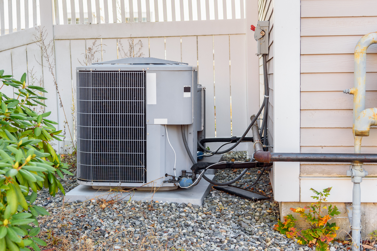 Outdoor air conditioning unit beside house and fence.